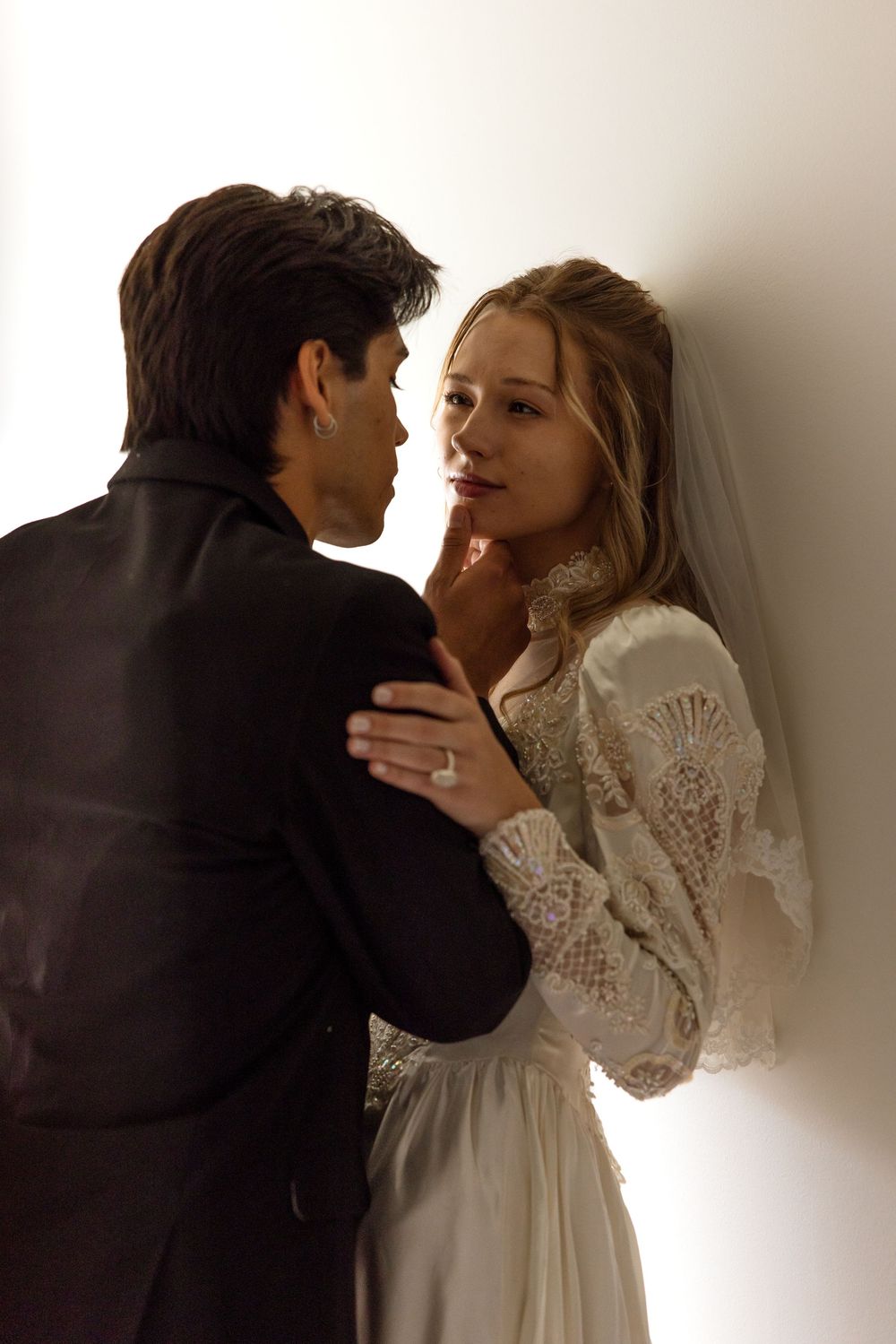 Romantic couple in vintage-inspired wedding attire share an intimate moment against a softly lit backdrop.