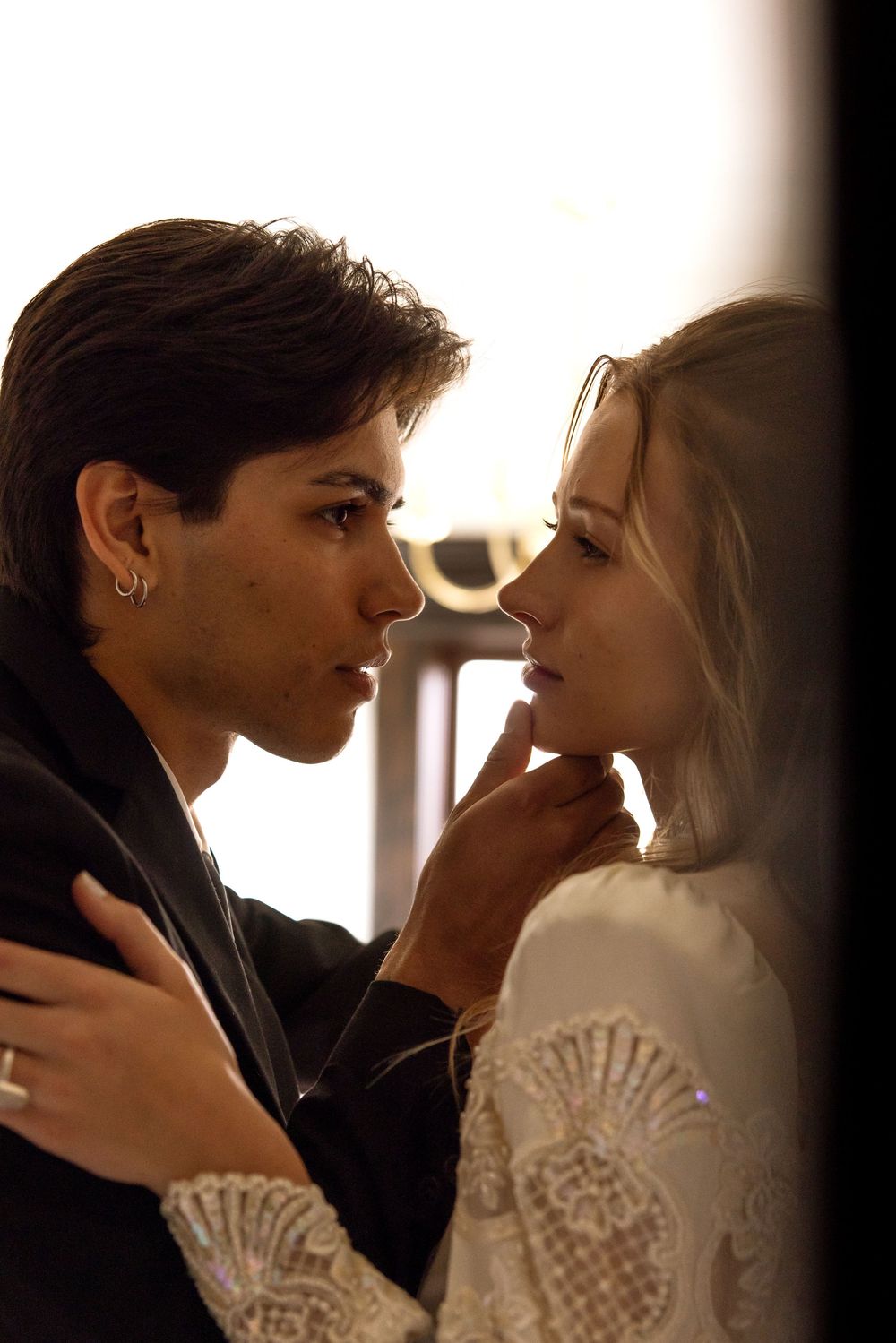 A romantic close-up of a couple in an intimate pose, with the woman wearing a white lace dress and the man in dark attire.