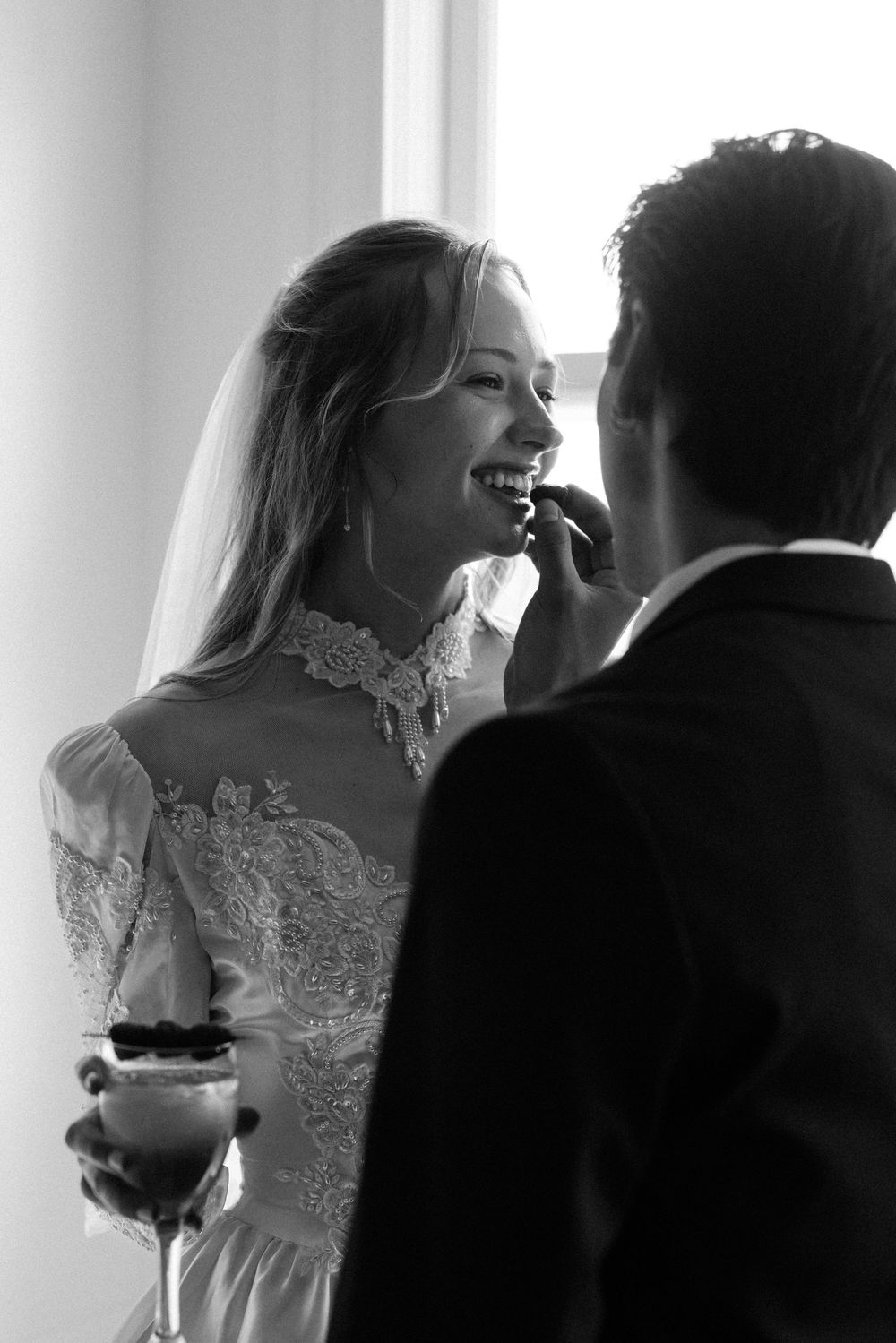 Black and white wedding photo of a couple sharing an intimate moment as bride laughs while holding a cocktail glass.