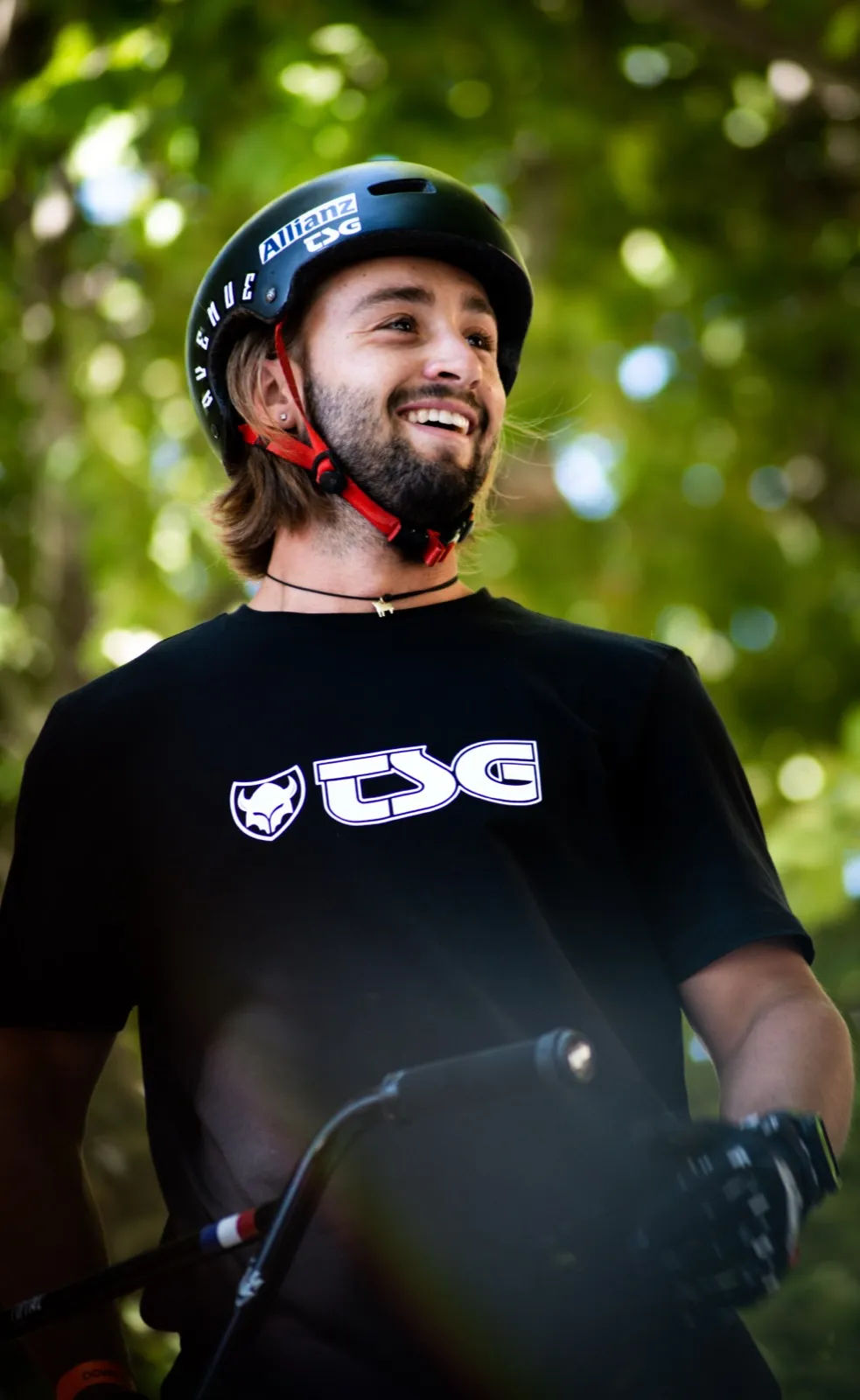 Portrait d’un rider en casque, t-shirt noir, sourire et lumière d’arrière-plan végétal.