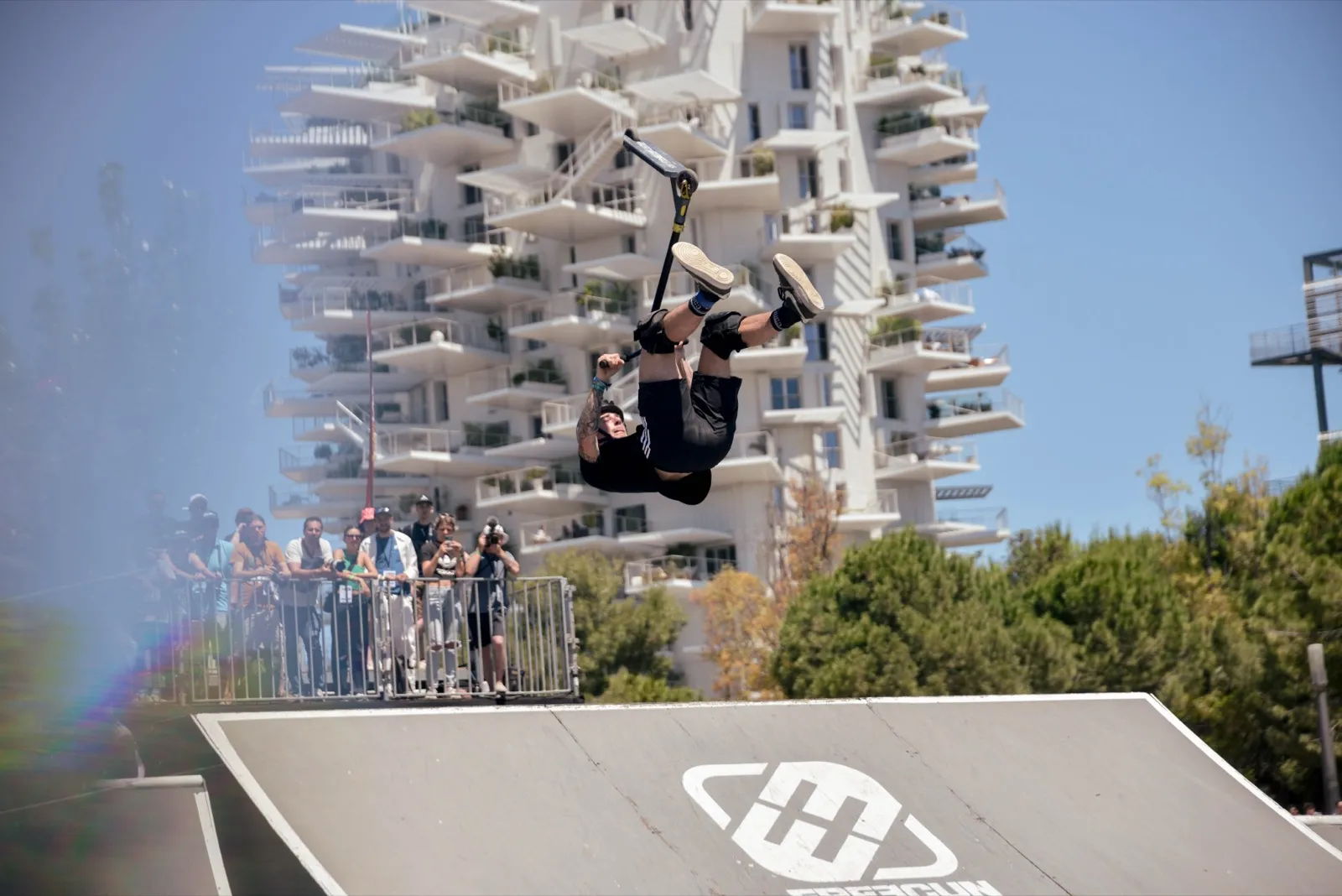 Rider en plein saut sur une rampe, avec la tour « Arbre blanc » de Montpellier en fond.