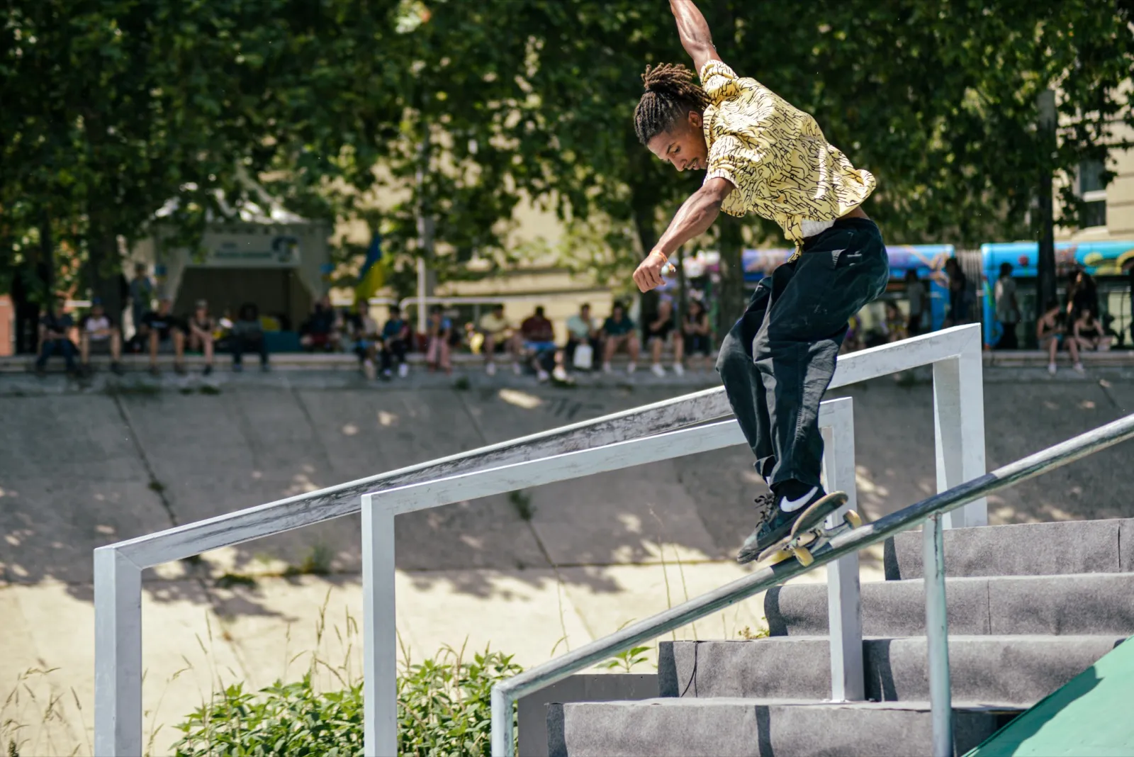Skateur en grind sur un rail, chemise à motifs et foule en arrière-plan.