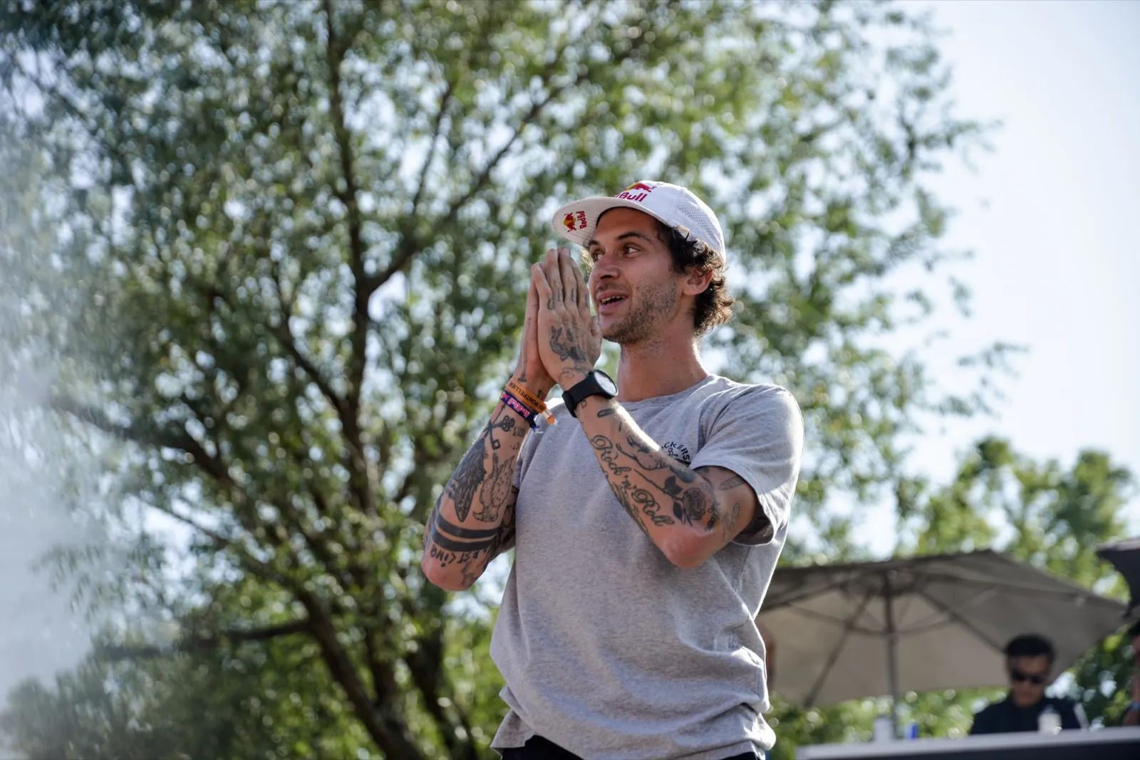 Rider applaudissant, bras joints, casquette blanche et tatouages visibles.