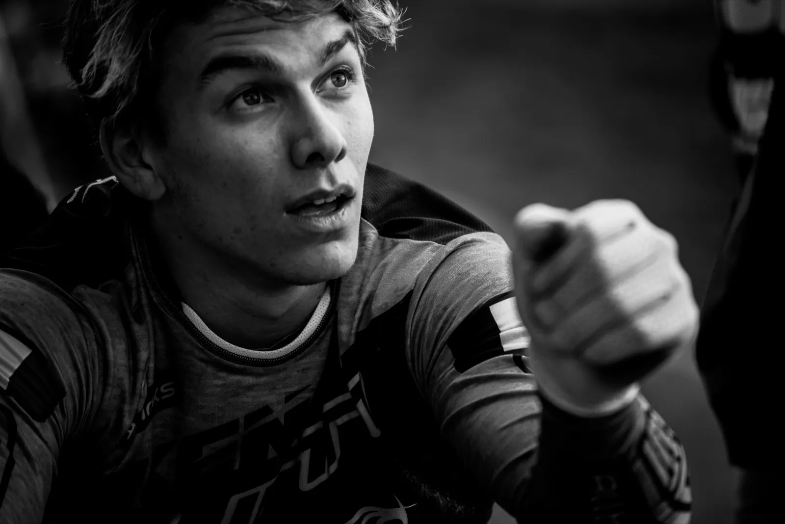 Portrait en noir et blanc d’un jeune rider BMX en pleine conversation, le regard vif et la main levée comme pour insister sur ses mots.