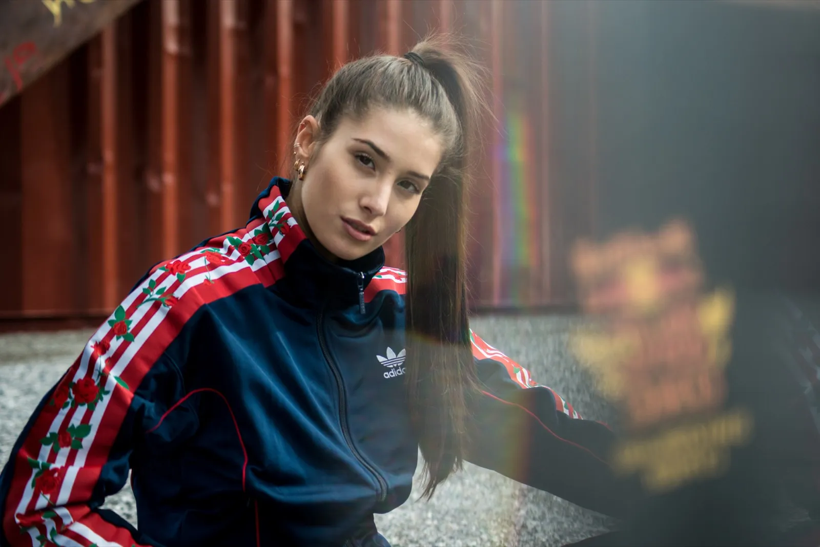 Portrait d’une jeune femme en survêtement Adidas x Red Bull, assise en extérieur, regard déterminé et franc vers l’objectif.