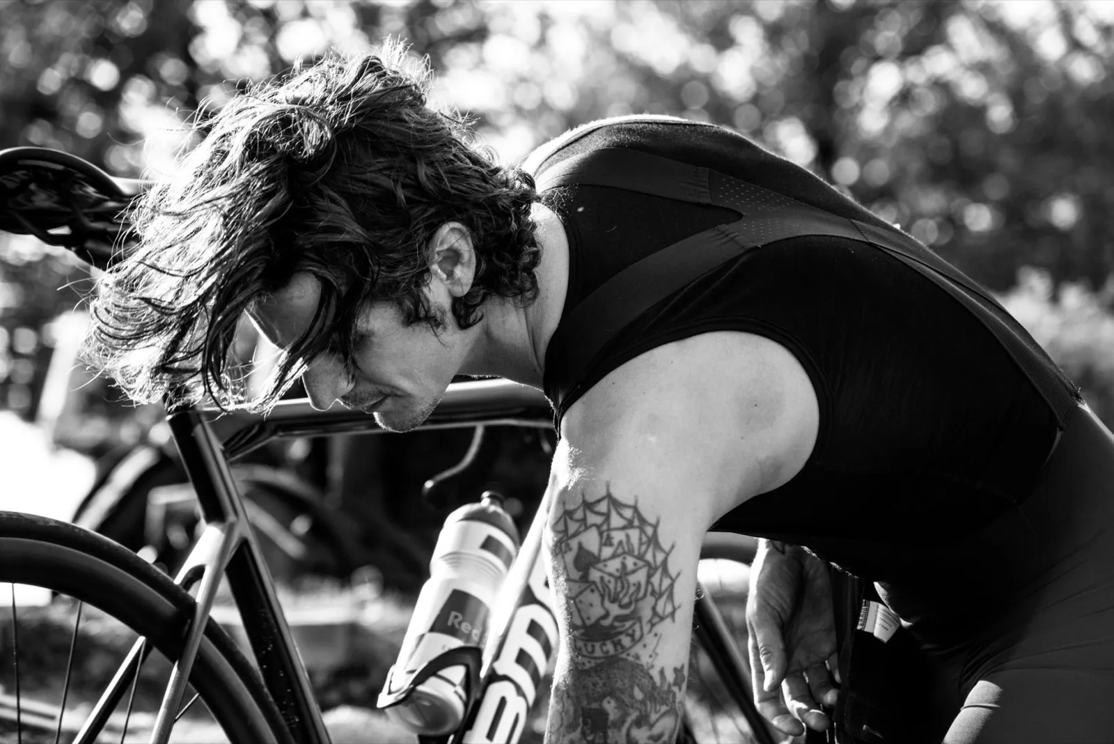 Cycliste concentré en noir et blanc, penché sur son guidon avec un bras tatoué, en plein effort ou récupération.