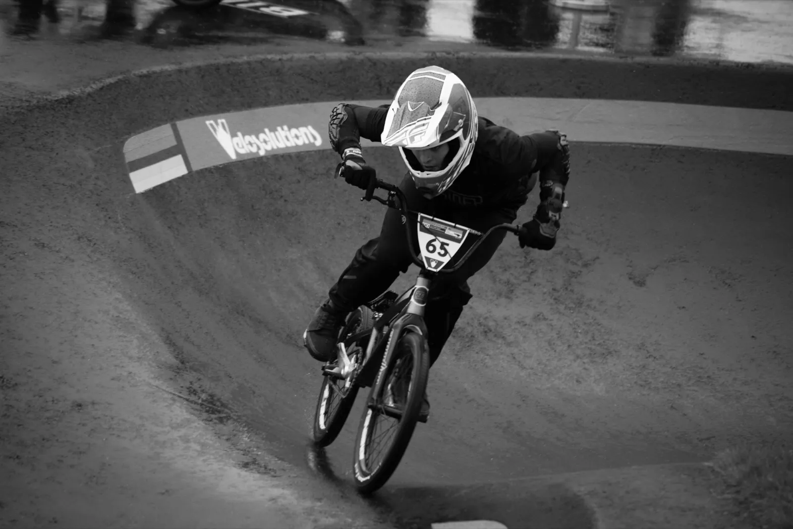 Photo en noir et blanc d’un jeune rider BMX dans une courbe, en pleine action avec le regard fixé sur la trajectoire.