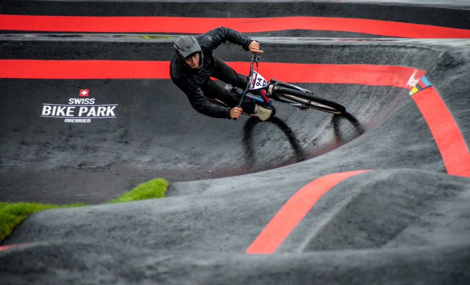 Rider BMX incliné dans un virage serré d’un bike park, capturé en pleine vitesse sur une piste marquée de lignes rouges.