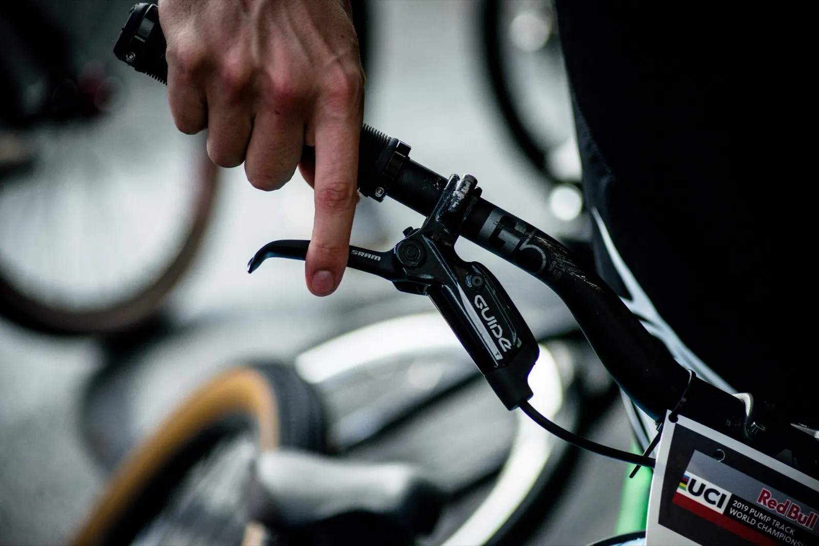 Main d’un rider tenant fermement le guidon de son vélo BMX, en arrière-plan flou de roues et de vélos.