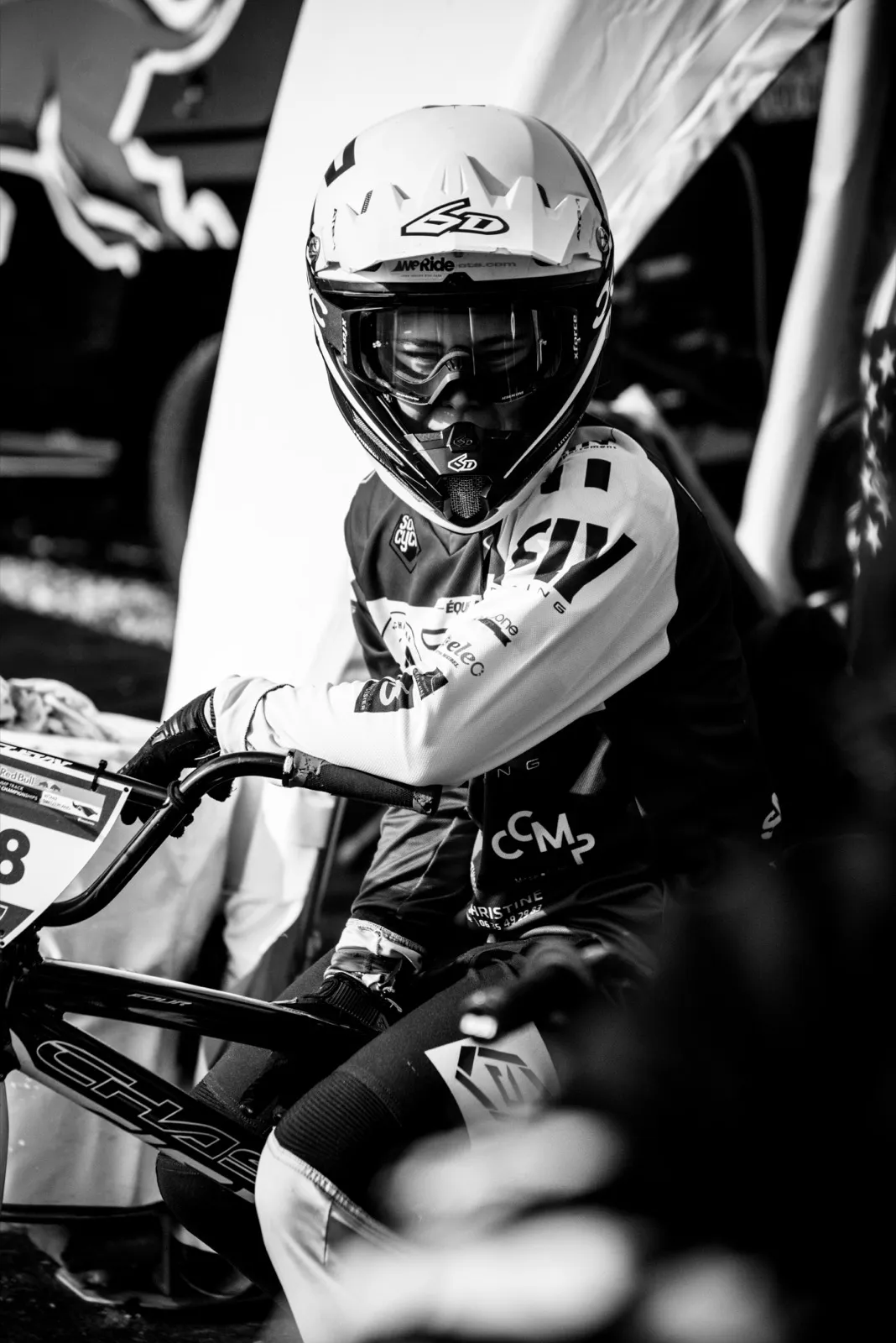 Photo en noir et blanc d’un jeune rider BMX, assis sur son vélo au bord de la piste, l’air concentré.