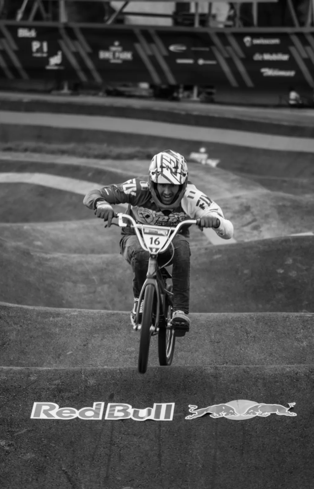 Rider BMX en plein saut au-dessus de la piste, capturé en vol avec une banderole Red Bull en arrière-plan.