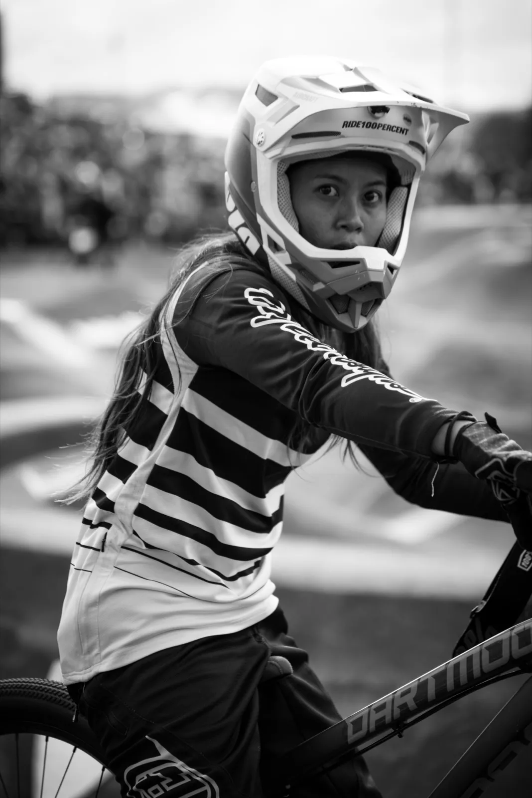 Portrait en noir et blanc d’un jeune rider BMX en tenue, casque intégral posé sur la tête, regard concentré.