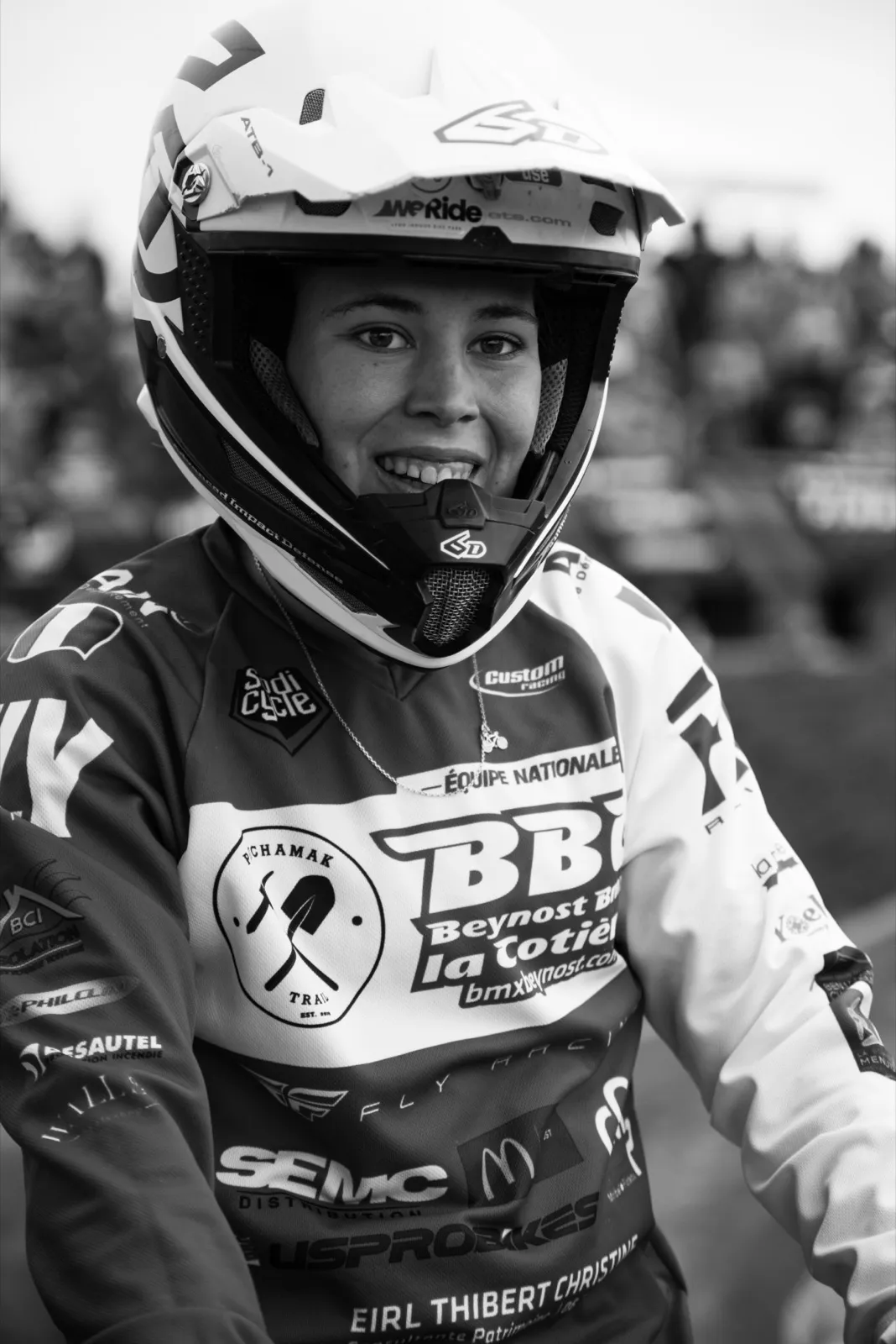 Portrait en noir et blanc d’un rider BMX en tenue de compétition, casque intégral Red Bull et sponsor BB.