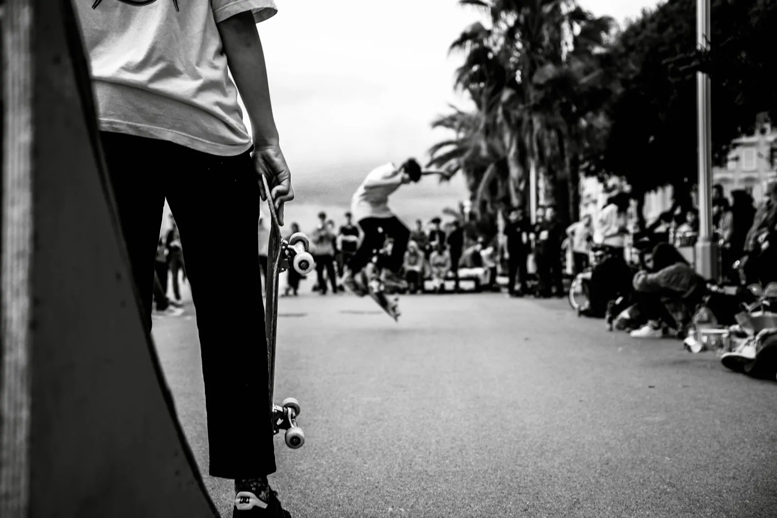 Scène de rue en noir et blanc, skateur s’élançant au loin entre deux silhouettes.