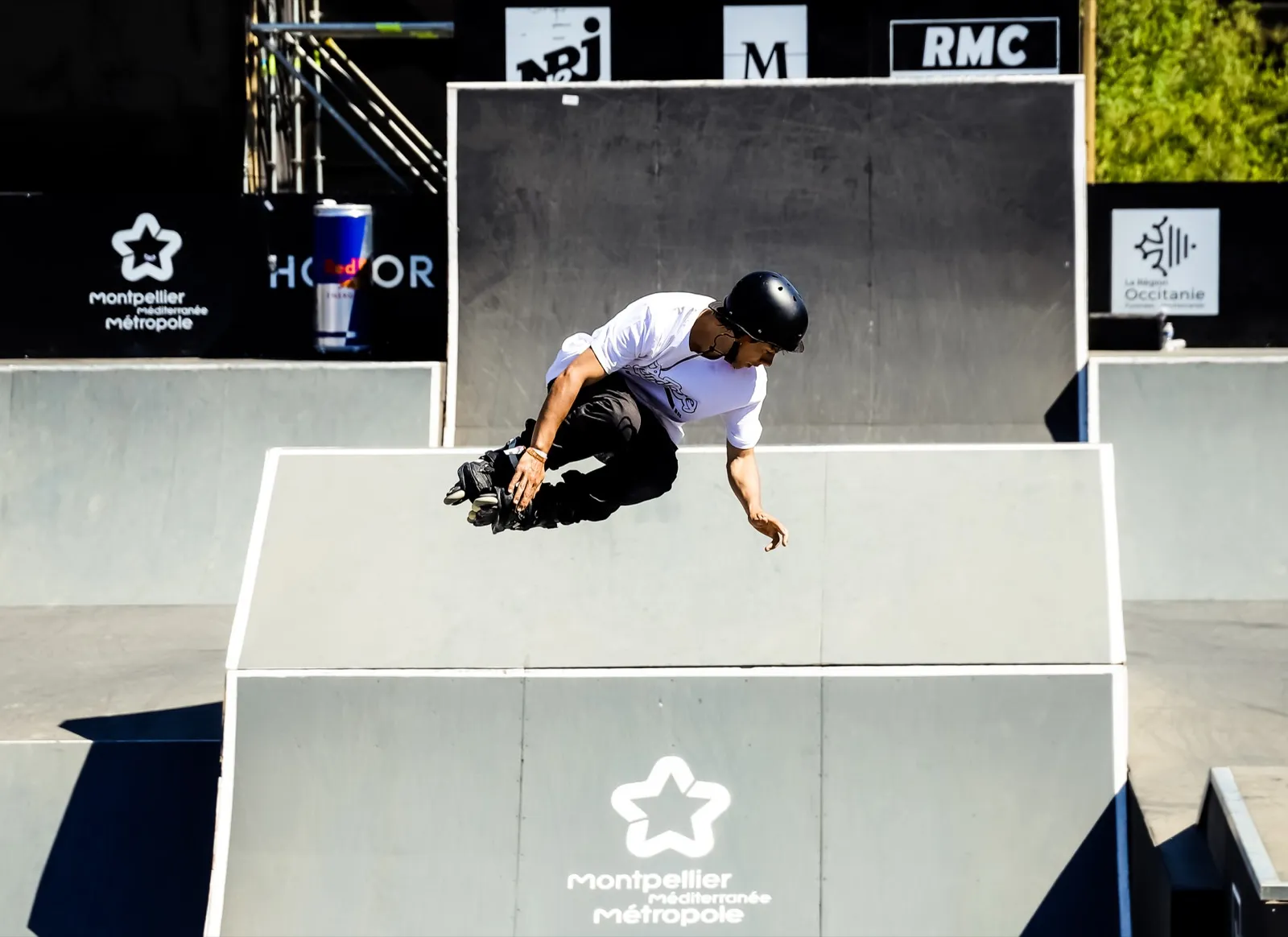 Rider effectuant une figure sur une rampe de skate lors d’un événement sponsorisé, en plein mouvement.