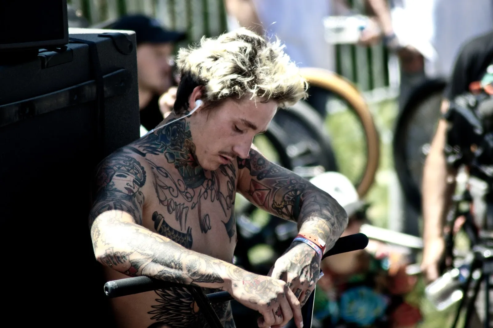 Portrait d’un rider tatoué, souriant en regardant son bras, entouré de vélos et d’autres riders.