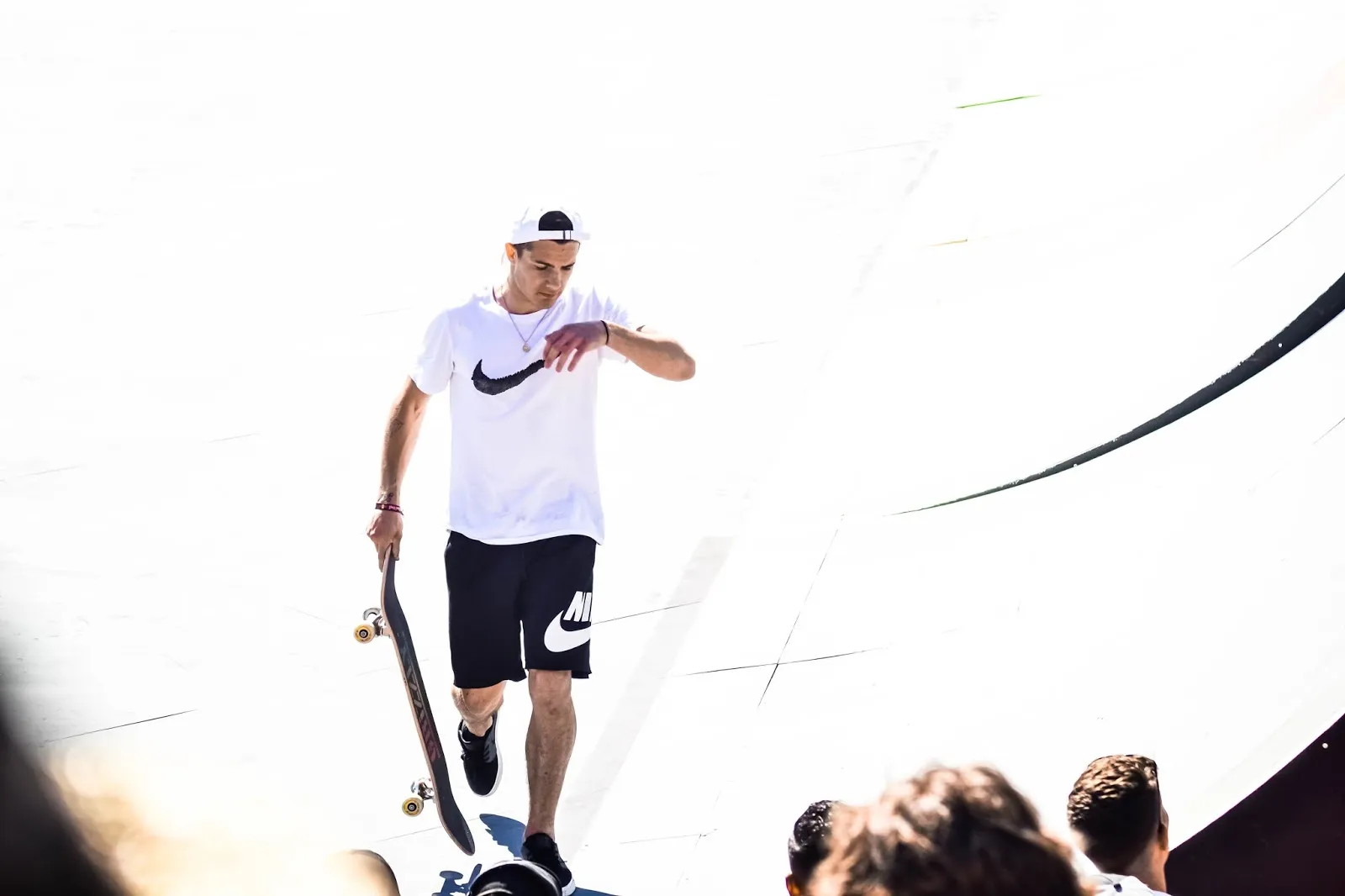 Rider en short blanc marchant sur une rampe de skate, skate à la main, sous une lumière vive.