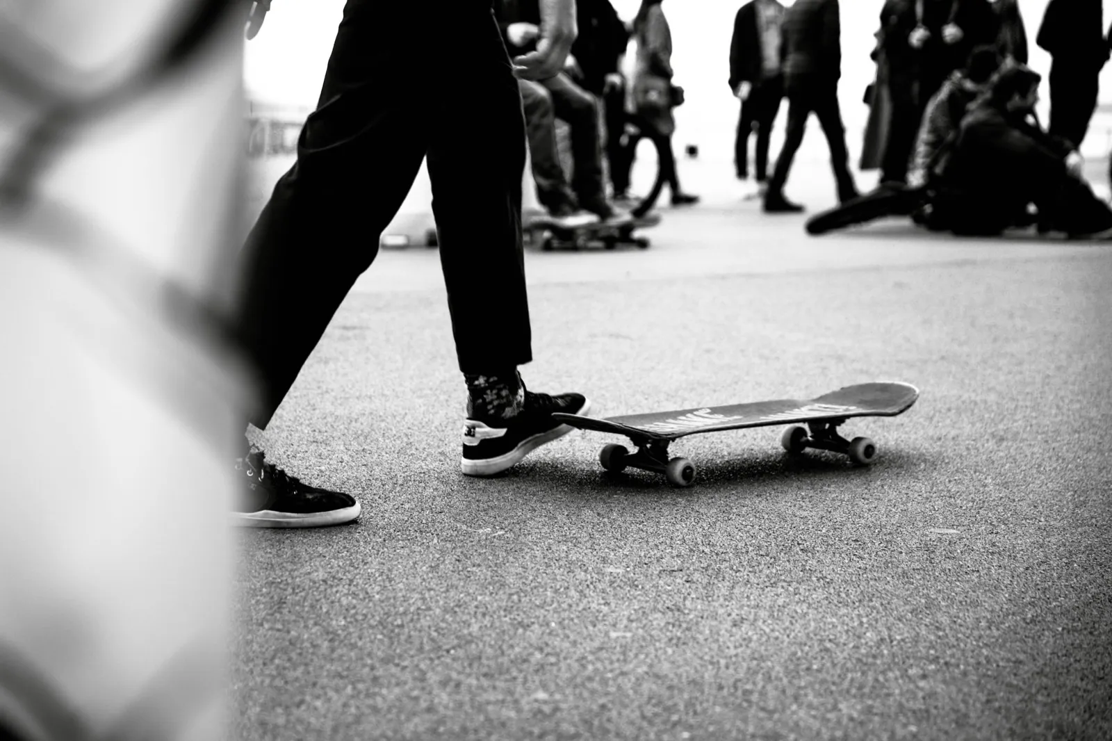 Plan au ras du sol d’un skate abandonné, avec silhouettes de passants en arrière-plan.
