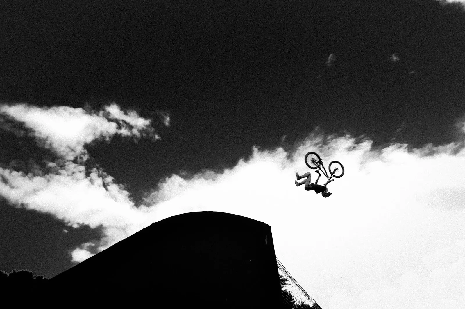 Rider BMX capté en plein vol, silhouette se découpant dans un ciel contrasté.