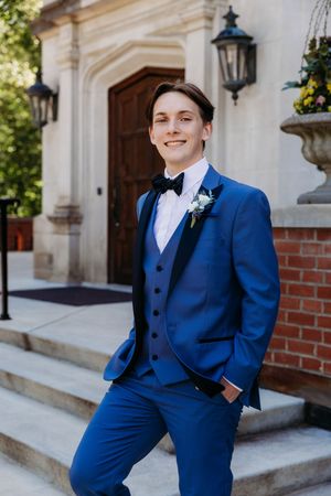 Someone in a stylish royal blue three-piece suit with boutonniere poses on church steps next to vintage lanterns.