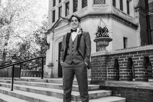 Black and white photo shows a person in formal suit standing on stone steps outside an ornate building.