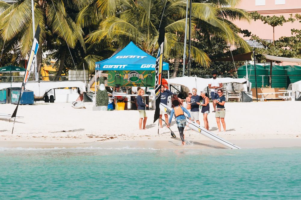 People enjoy a sunny day of water activities on a tropical beach with palm trees and tents near turquoise waters.