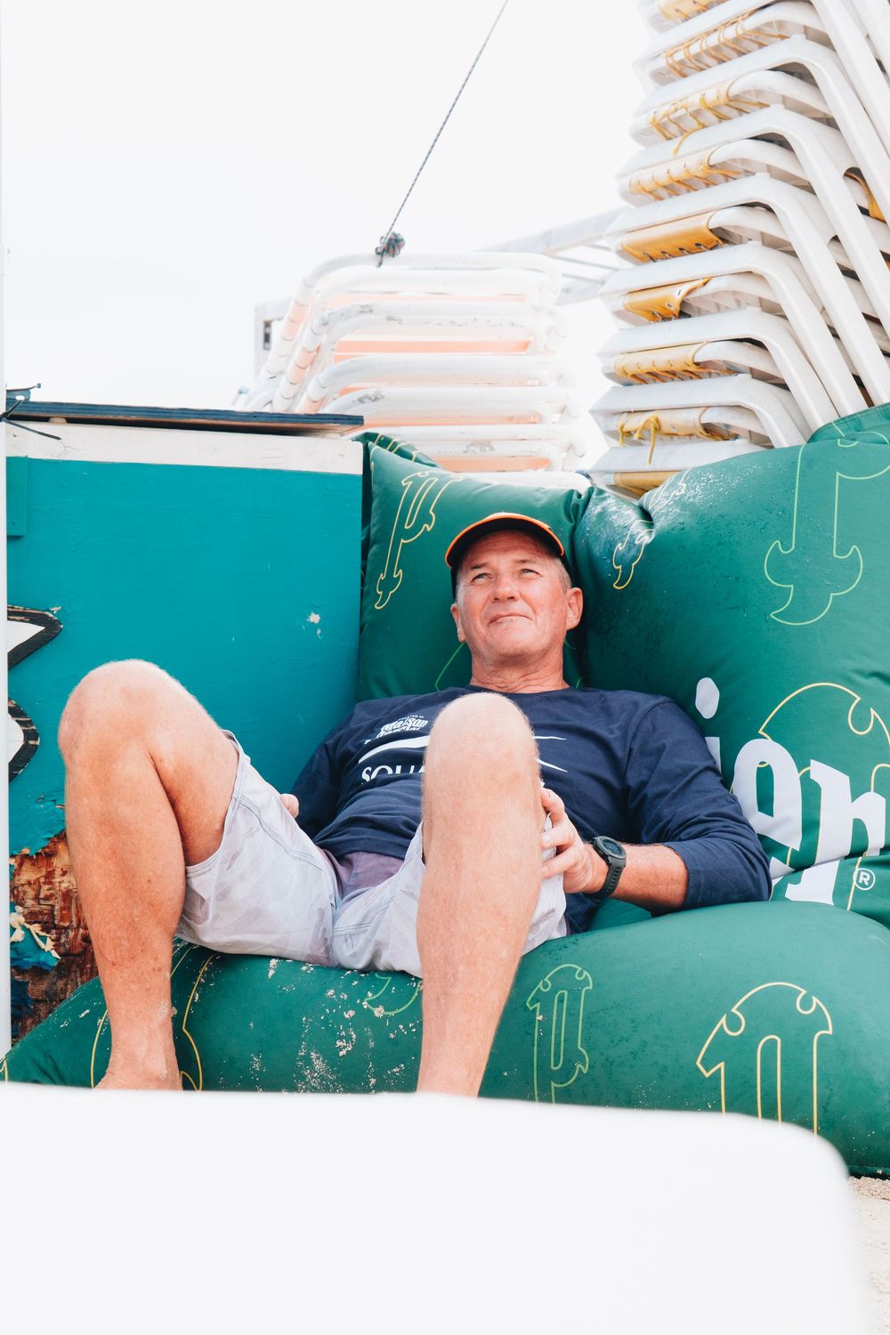 Person relaxing on a green bench with stacked white chairs visible in the background.