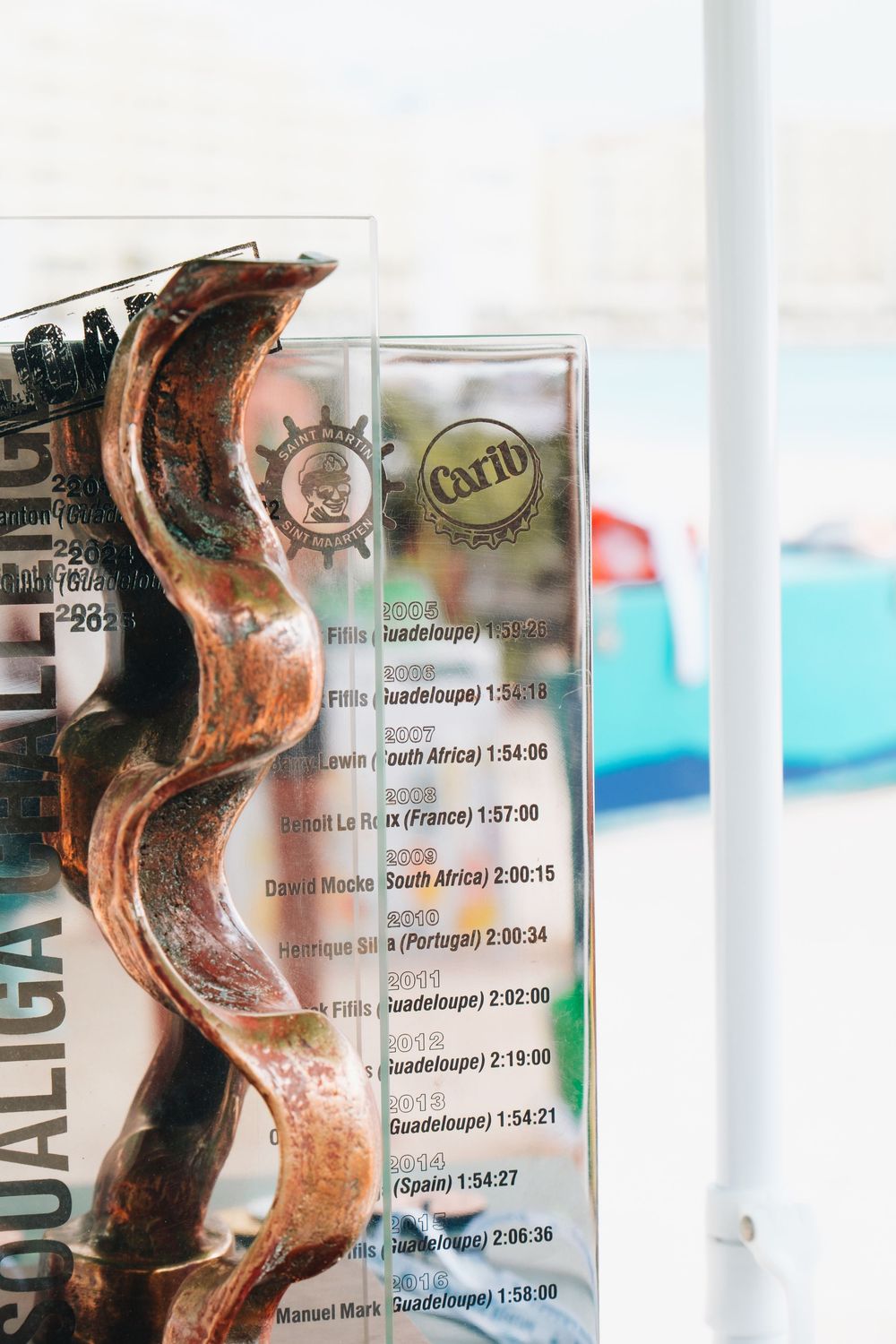 Glass beside a curved metal sculpture at a tropical bar or restaurant with drink menu visible.
