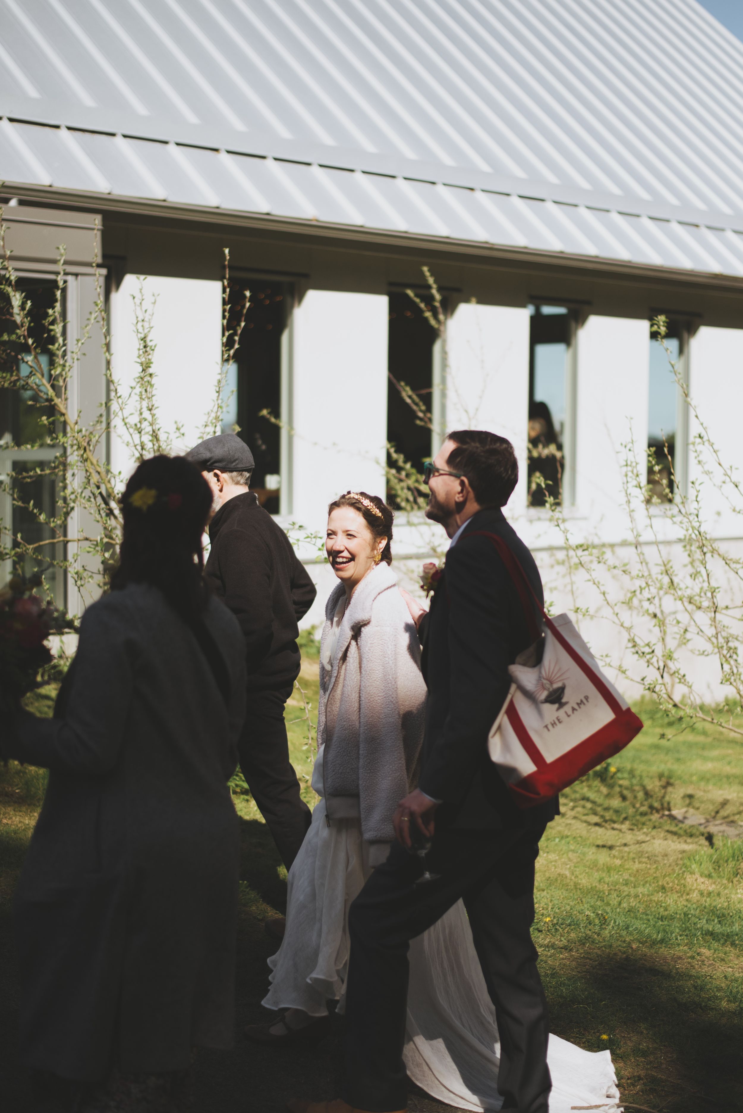 A group of people in formal attire share a candid moment outdoors near a white building in natural lighting.