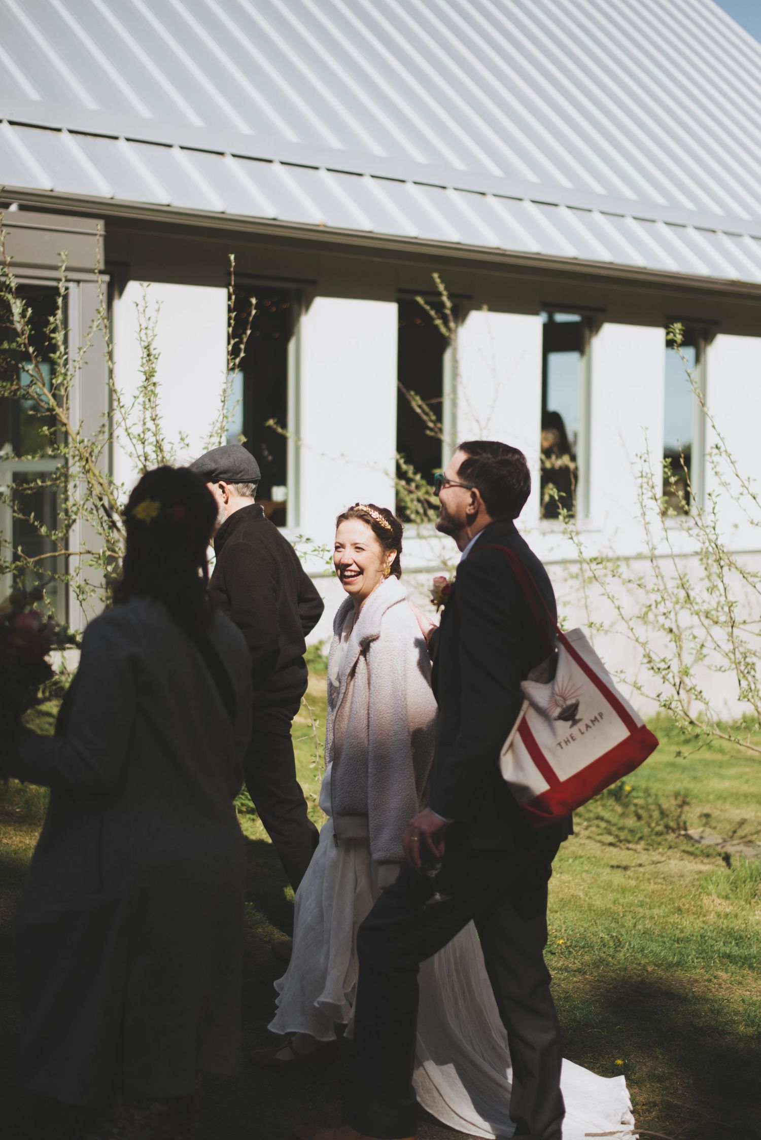 A group of people in formal attire share a candid moment outdoors near a white building in natural lighting.