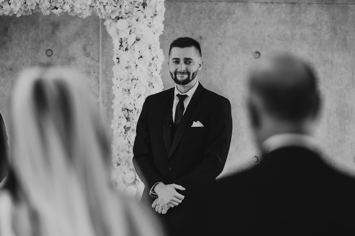 Black and white photo showing an emotional wedding ceremony moment as a groom reacts during the vows.