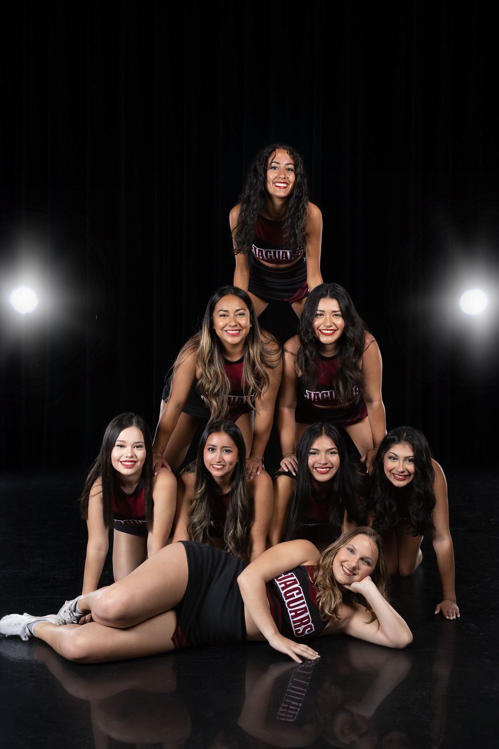 Dance team members in matching black outfits pose together on dark stage with dramatic lighting.