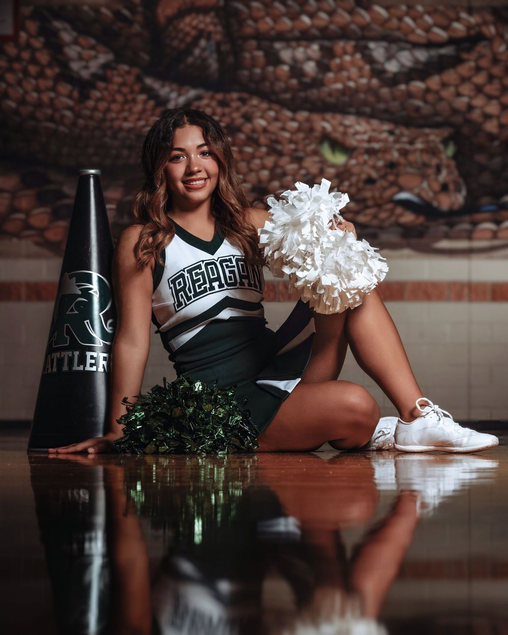 Creative cheerleader photo shoot with green bottle reflection on shiny floor surface showing dynamic poses and spirit.