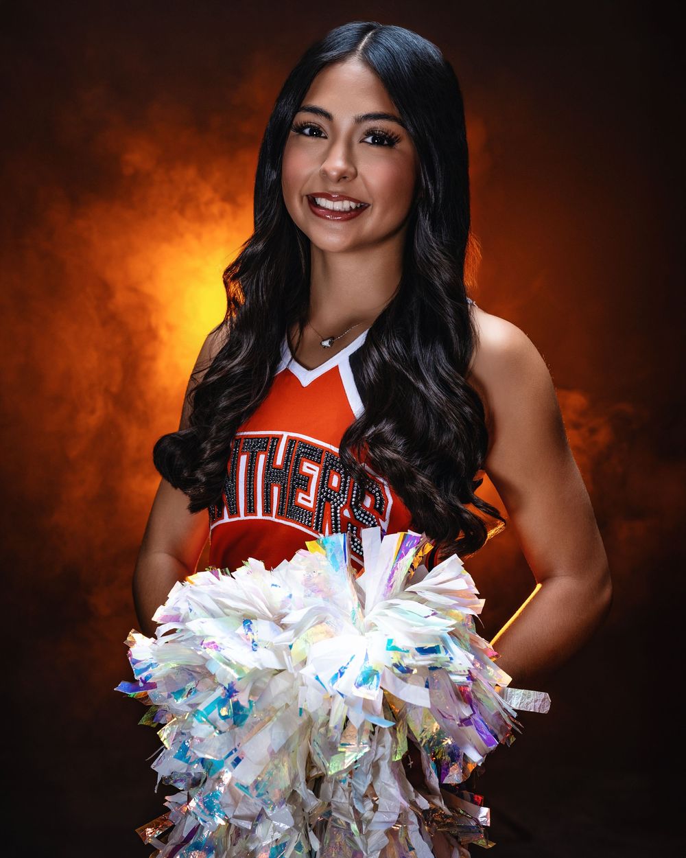 Cheerleader in an orange Tigers uniform holds a sparkly white and iridescent pom-pom against a dark orange background.