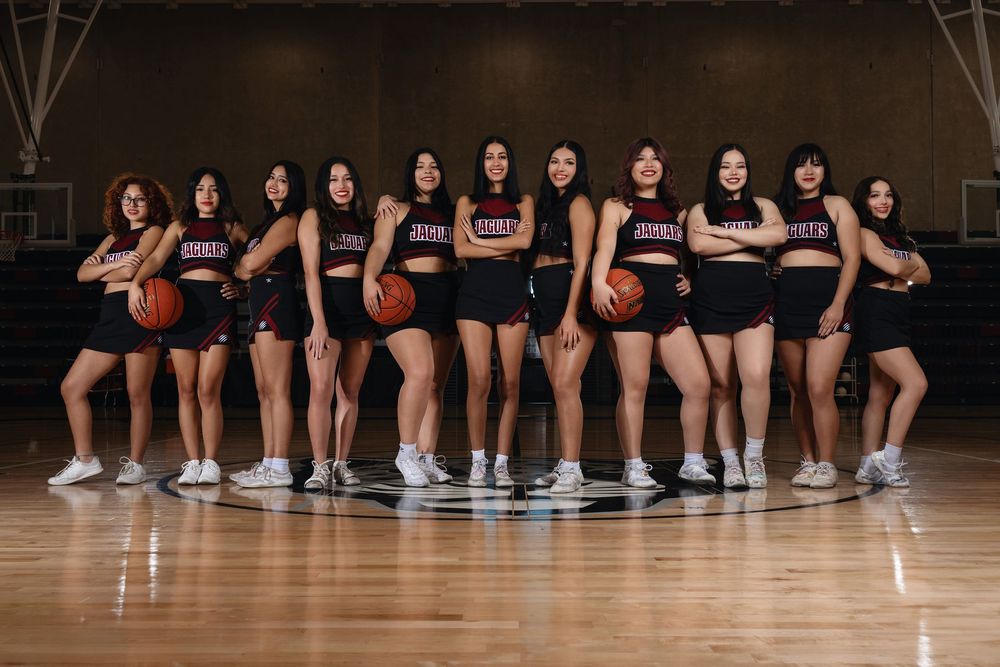 Basketball team poses with balls in matching black uniforms on indoor court.