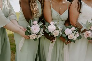 Close-up of bridesmaids holding pink rose bouquets in sage green dresses.