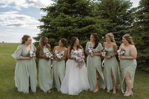 Wedding party in mint green dresses poses casually on grass with pine trees in background.