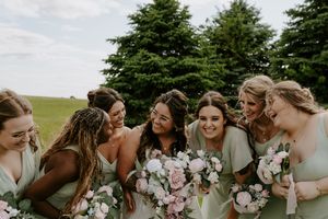 Bridal party laughs together while holding pink and white bouquets.