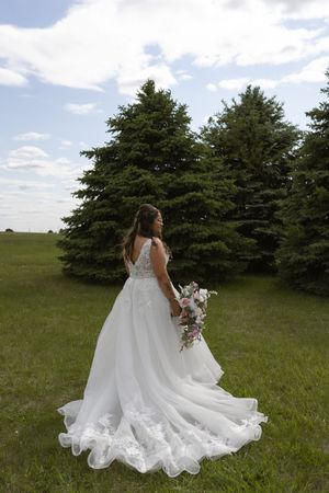 Flowing white wedding dress trails beautifully across green grass field.