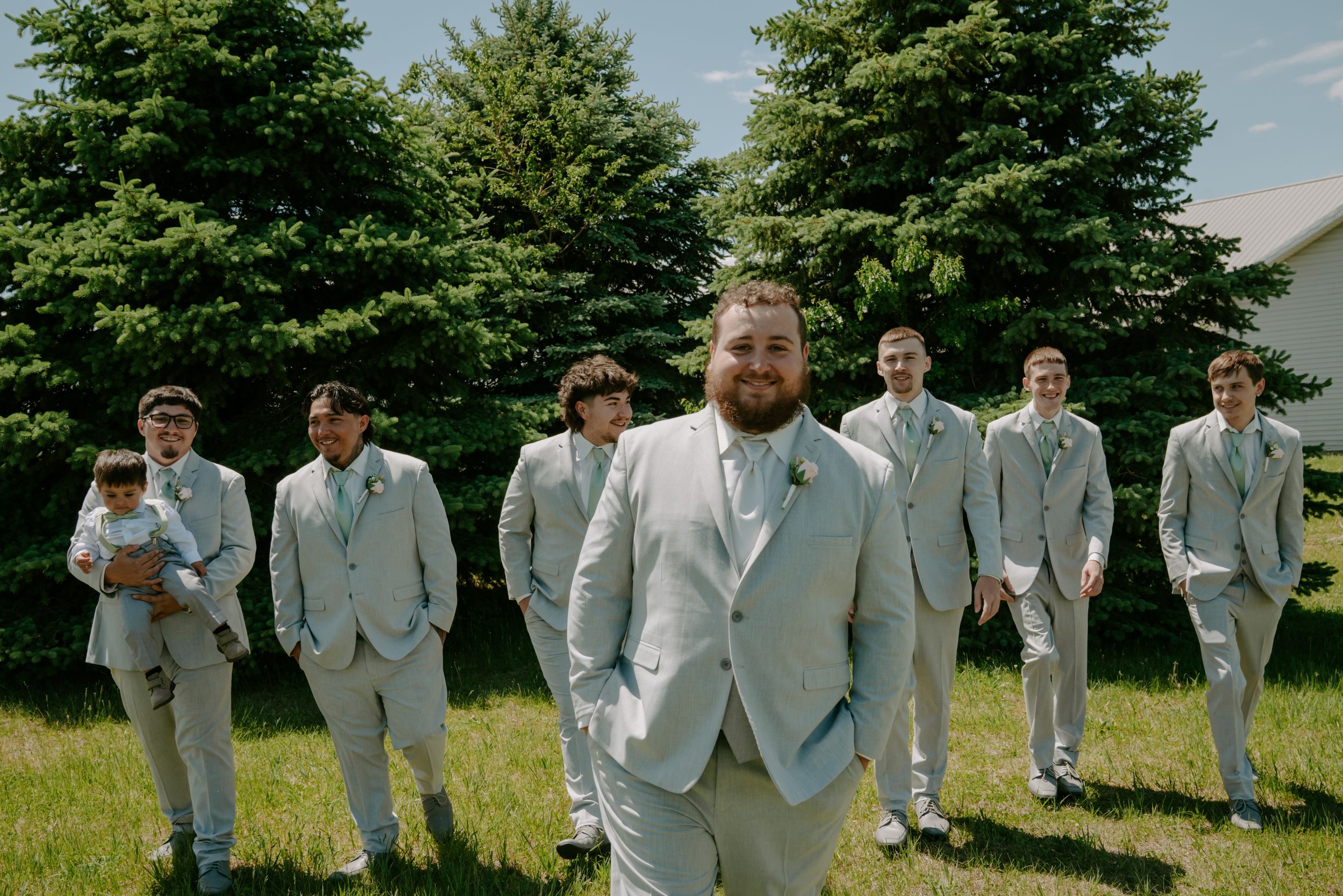Wedding party members in matching gray suits pose casually outdoors.
