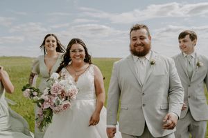 Wedding party members in light gray suits walk together on grass field.
