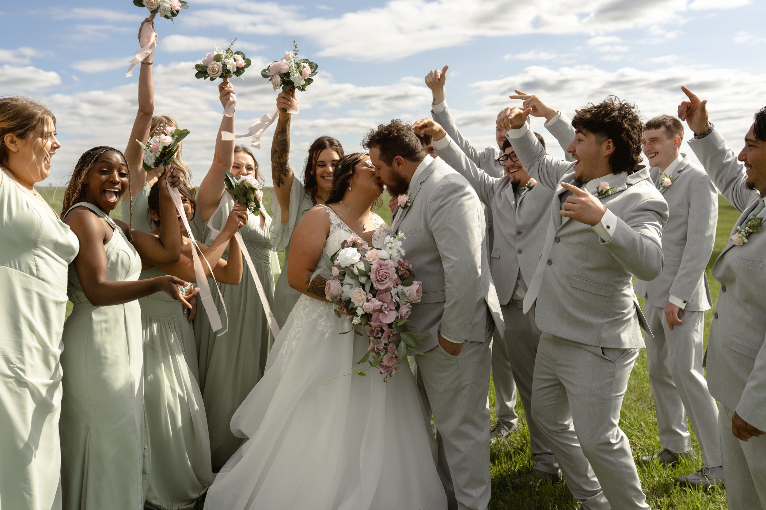 Joyful wedding party celebrating outdoors in light gray and white attire.