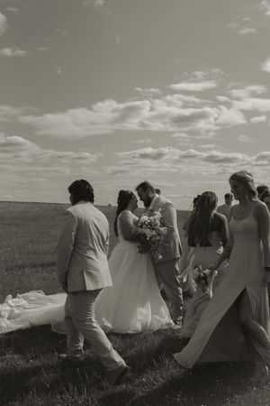 Black and white photo of wedding party posing together in an open field under cloudy skies.