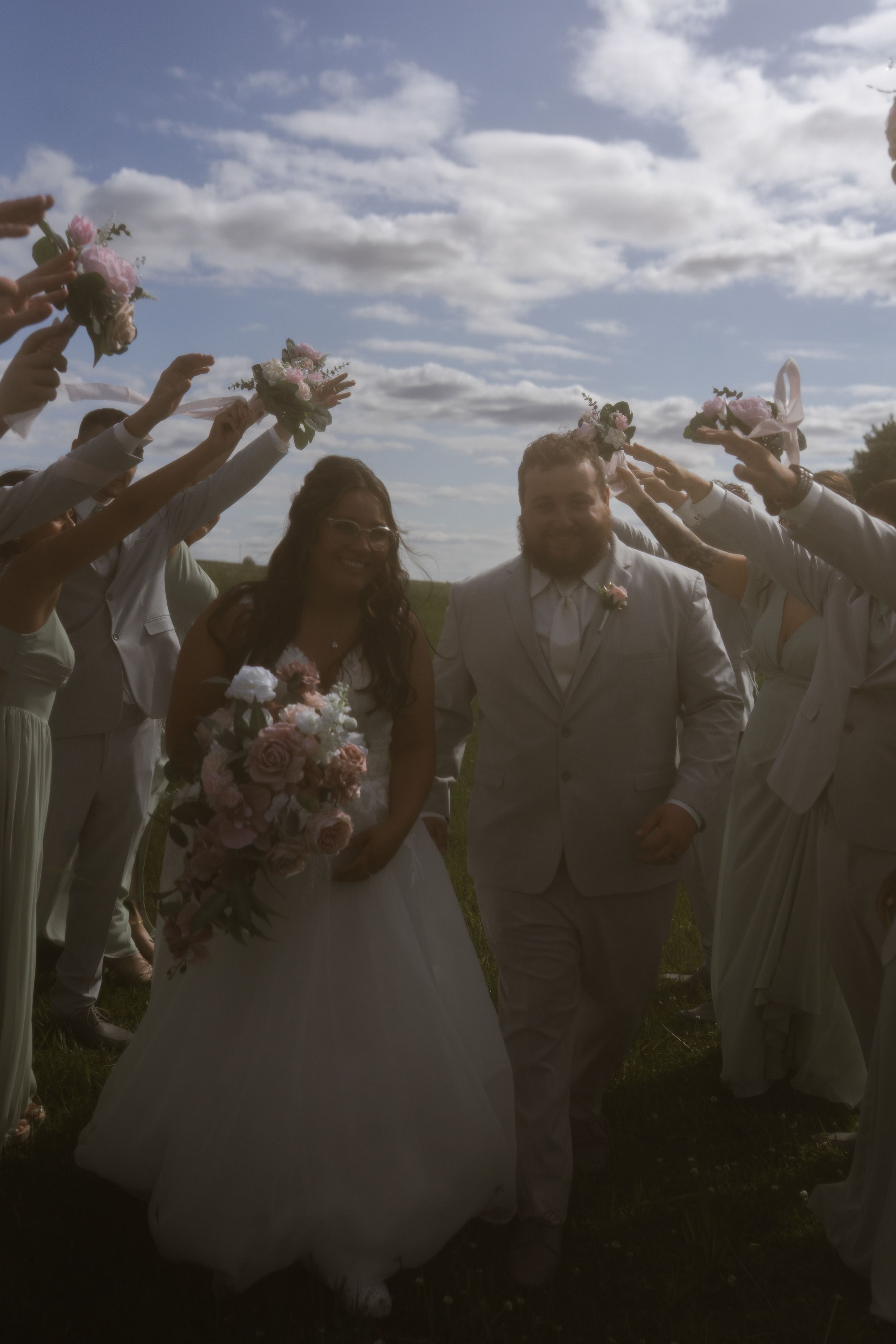 Wedding party members jumping and celebrating against a bright cloudy sky.