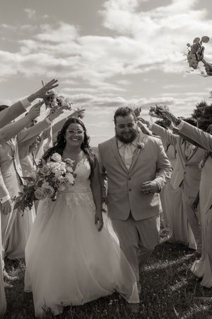 Wedding party members in light colored attire celebrate with raised arms outdoors.
