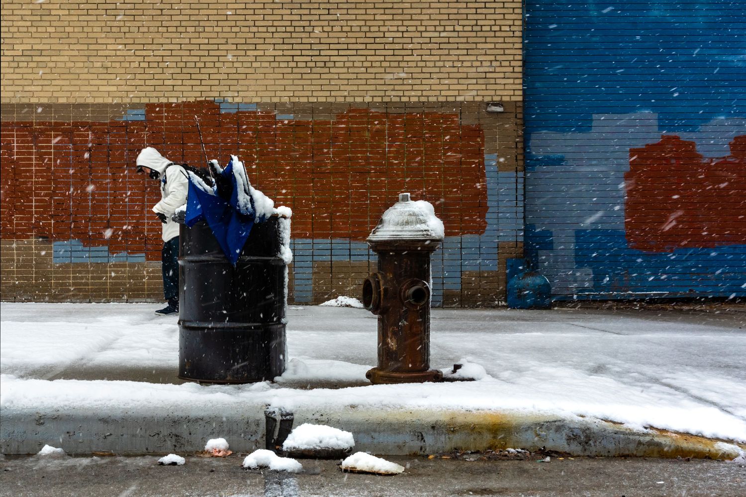 Snow-covered fire hydrants against brick wall in urban setting.