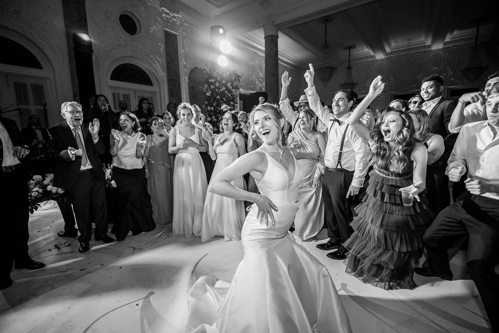 Wedding guests dance and celebrate on a dark dance floor under venue lighting.