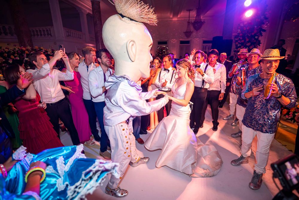Energetic dancers celebrate at a lively reception with colorful purple lighting and a large mascot character on the dance floor.