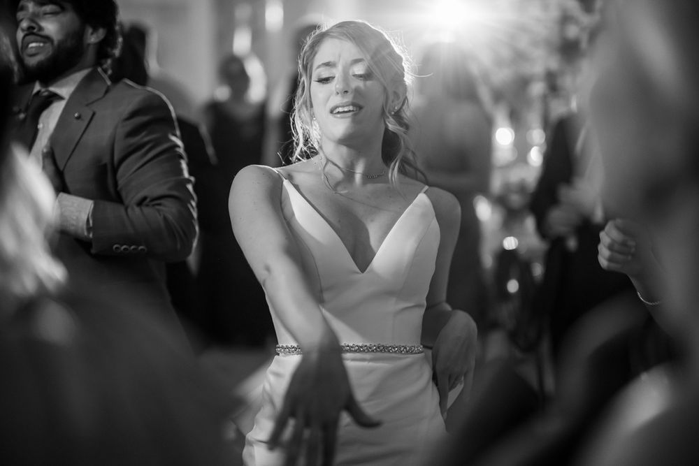 A bride in a sleek white dress dances joyfully at her wedding reception in a black and white photo.