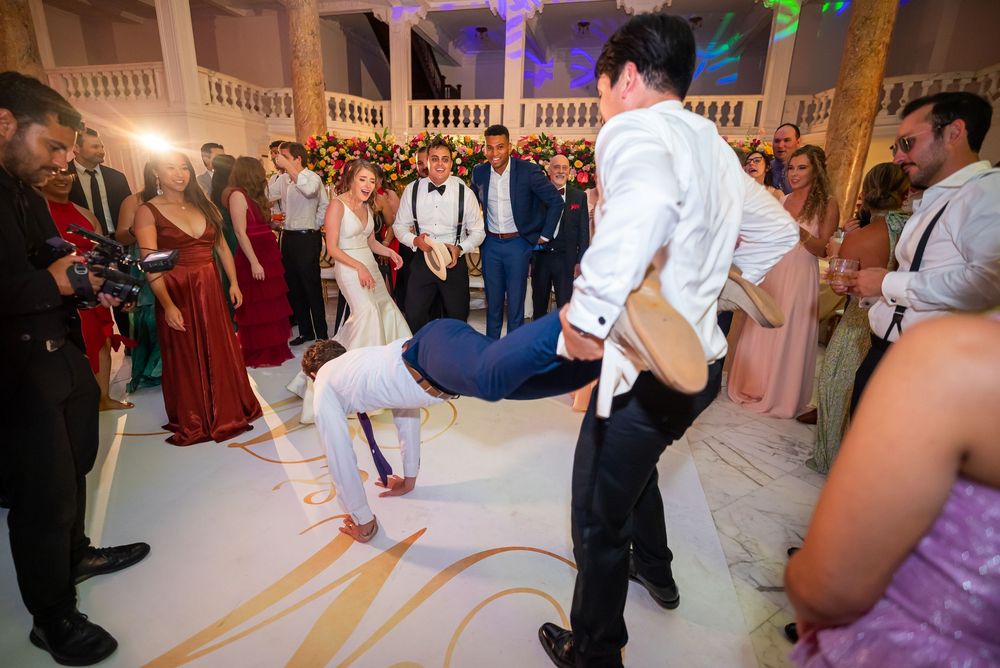 A couple dancing energetically during a wedding reception with guests cheering in an elegant ballroom.